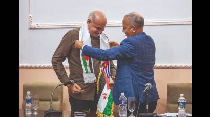 El embajador saharauí en Cuba, Omar Bulsan, coloca la banda con las banderas de la RASD y Cuba a Ricardo Ronquillo, presidente de la UPEC.